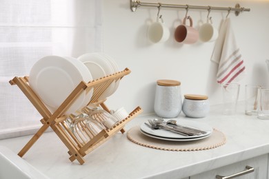 Drying rack with clean dishes on light marble countertop in kitchen