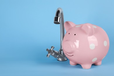 Photo of Water scarcity concept. Piggy bank and tap on light blue background, space for text