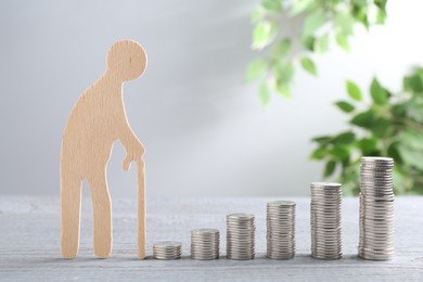 Photo of Pension savings. Figure of senior man and stacked coins on grey wooden table