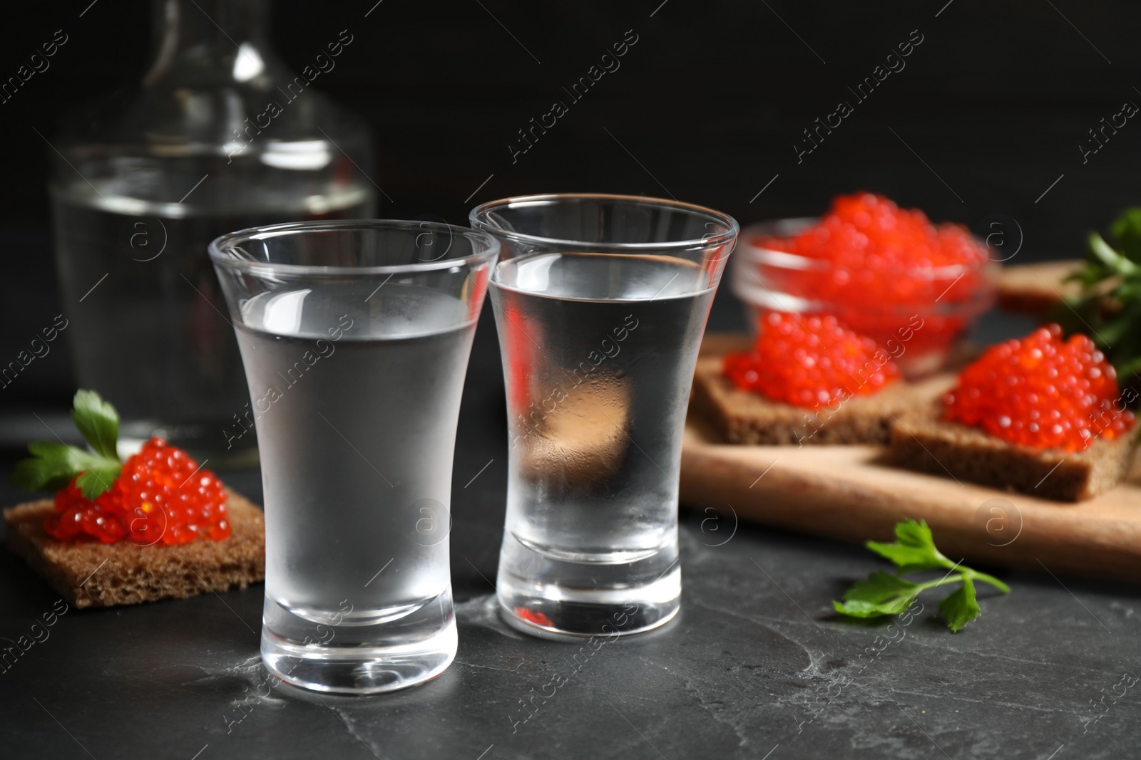 Photo of Cold Russian vodka and sandwiches with red caviar on black table, closeup