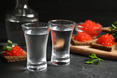 Photo of Cold Russian vodka and sandwiches with red caviar on black table, closeup