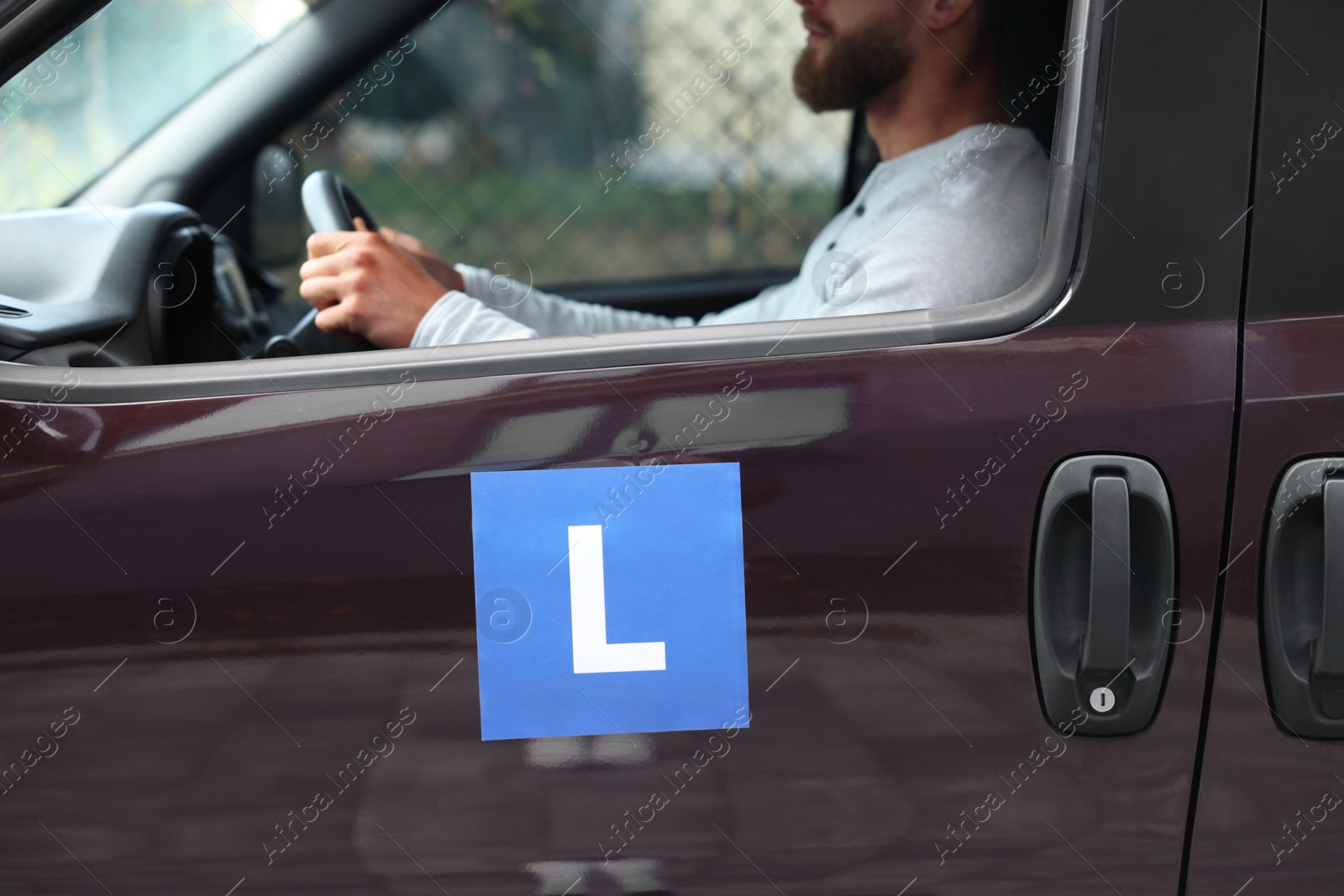 Photo of Learner driver driving car with L-plate, view from outside. Driving school