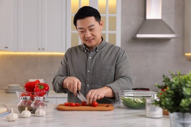 Cooking process. Man cutting fresh tomatoes at countertop in kitchen