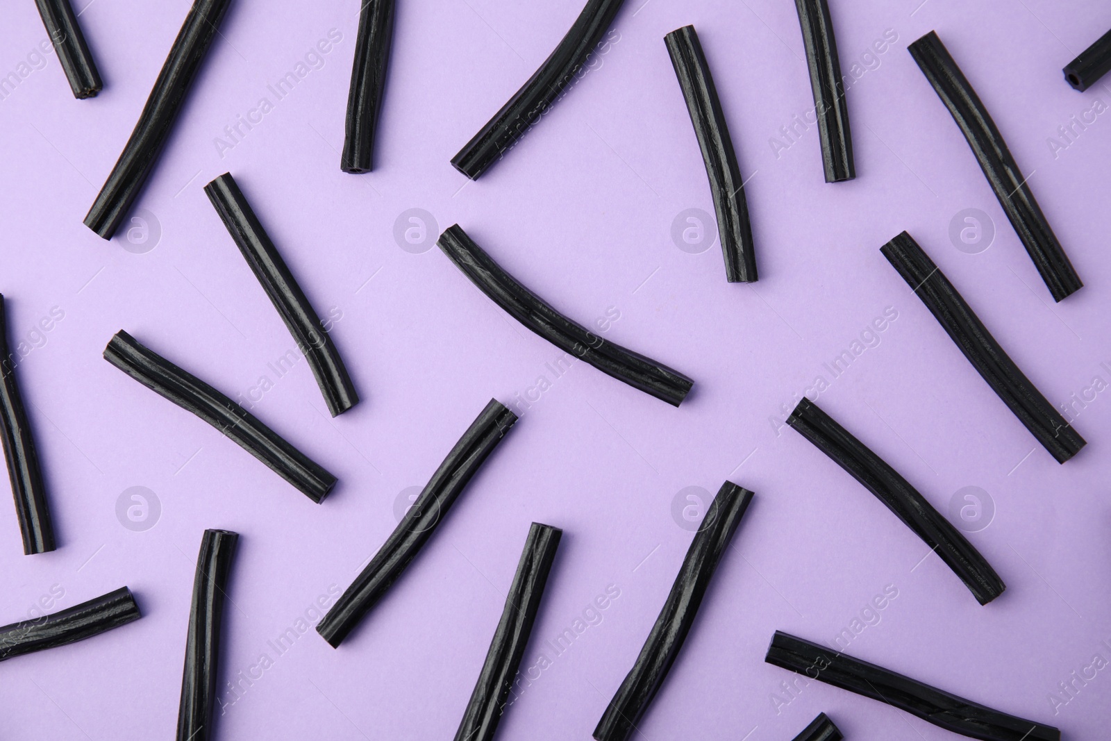 Photo of Tasty black liquorice candies on violet background, flat lay