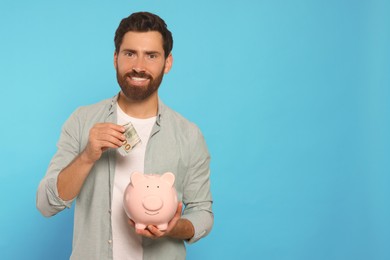 Photo of Happy man putting money into piggy bank on light blue background, space for text