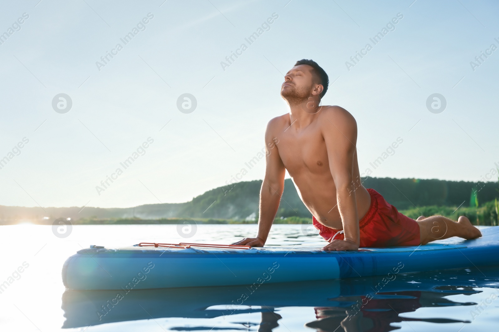 Photo of Man practicing yoga on light blue SUP board on river at sunset