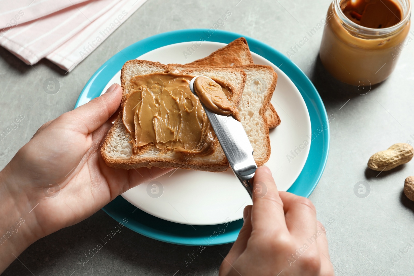 Photo of Woman spreading peanut butter on toast bread at table, closeup