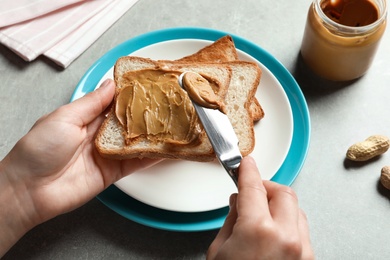 Photo of Woman spreading peanut butter on toast bread at table, closeup