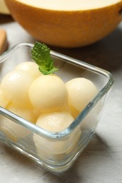 Photo of Melon balls with mint in glass bowl on table, closeup