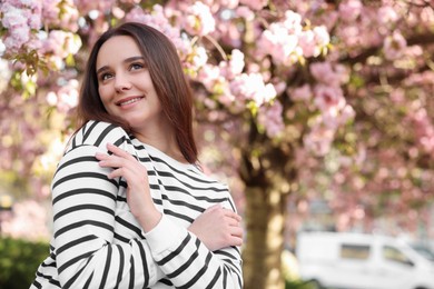 Beautiful woman near blossoming tree on spring day, space for text