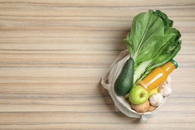 Cloth bag with fruits, vegetables and bottle of juice on wooden background, top view. Space for text