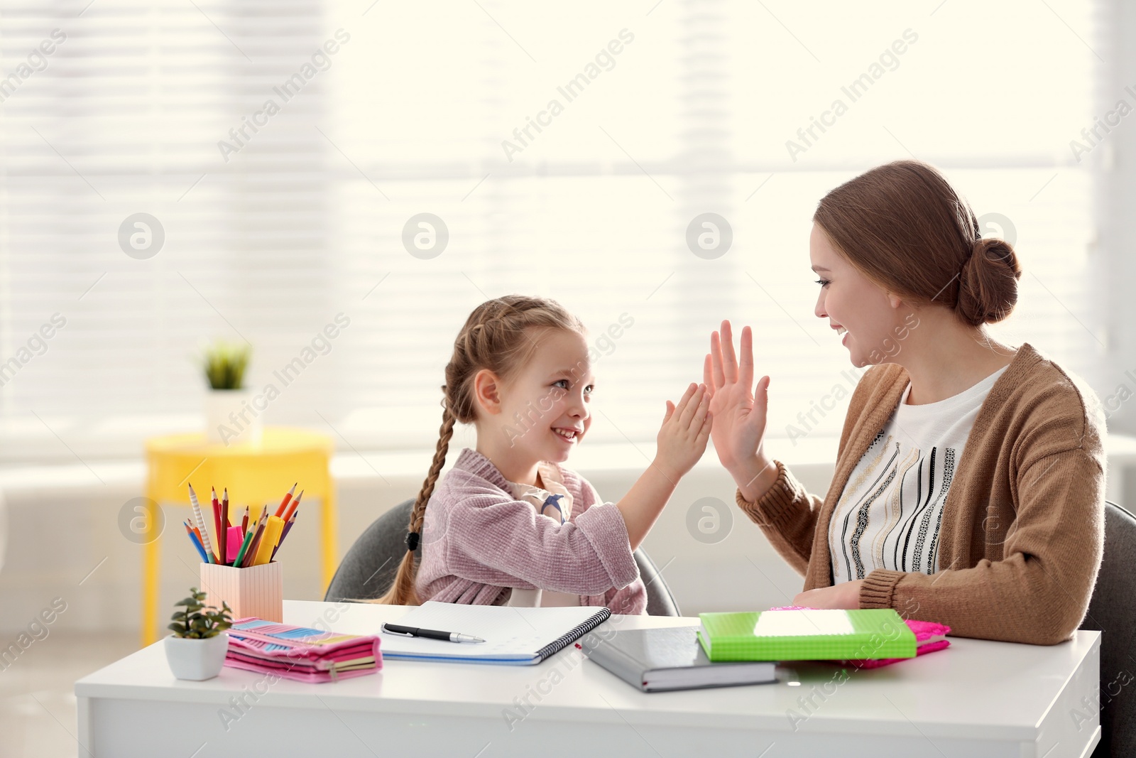 Photo of Mother and daughter doing homework together at table indoors