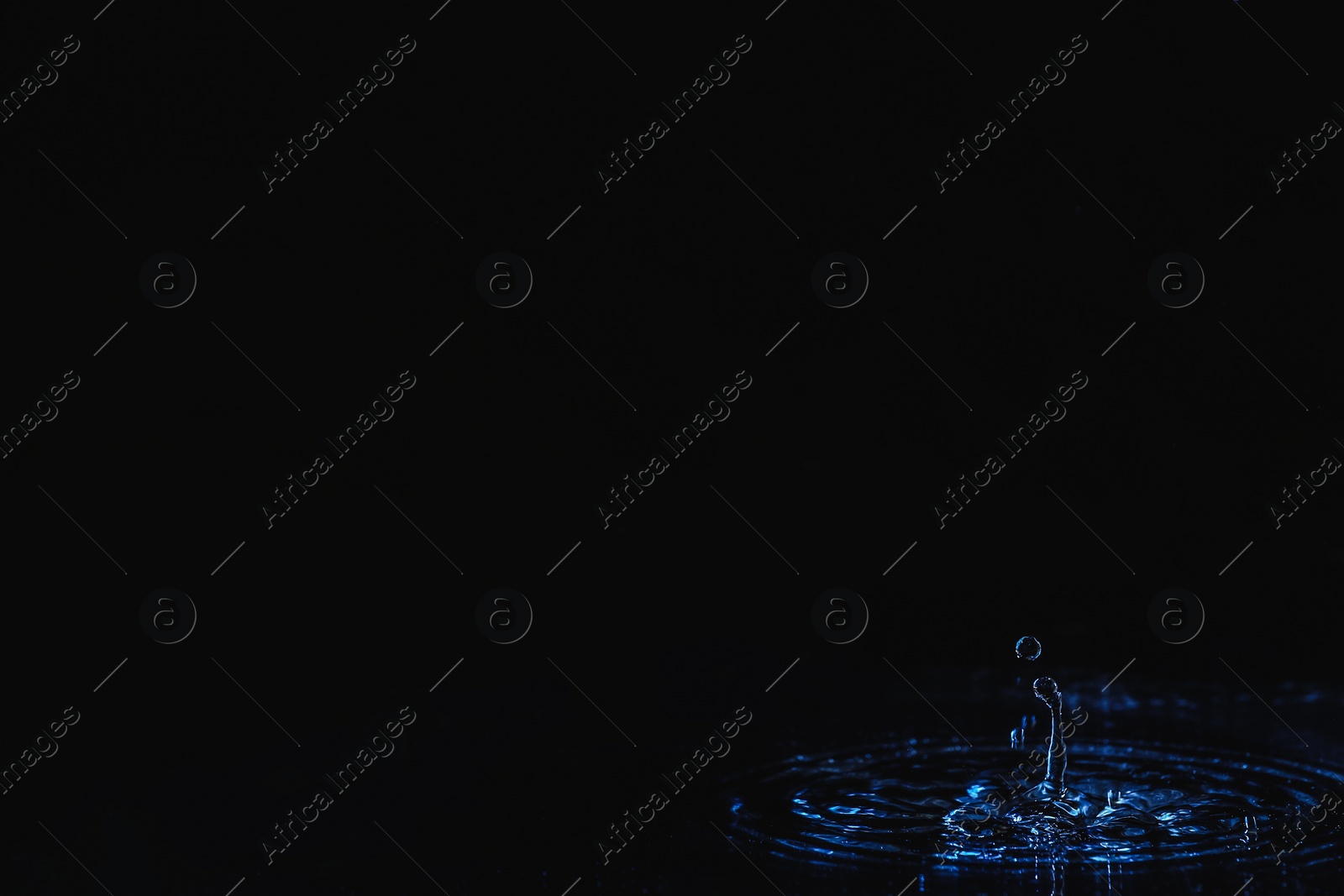 Photo of Rain drop falling down into puddle on dark background, space for text