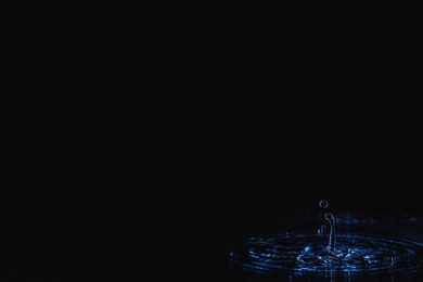 Photo of Rain drop falling down into puddle on dark background, space for text