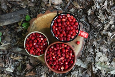 Photo of Dishes with tasty wild strawberries on stump outdoors, top view