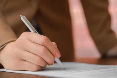 Photo of Woman signing documents at wooden table in office, closeup. Space for text