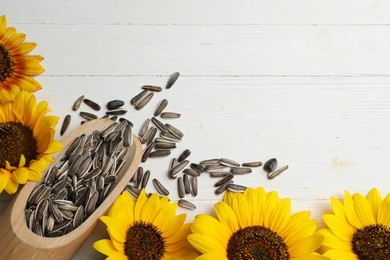 Photo of Raw sunflower seeds and flowers on white wooden table, flat lay. Space for text