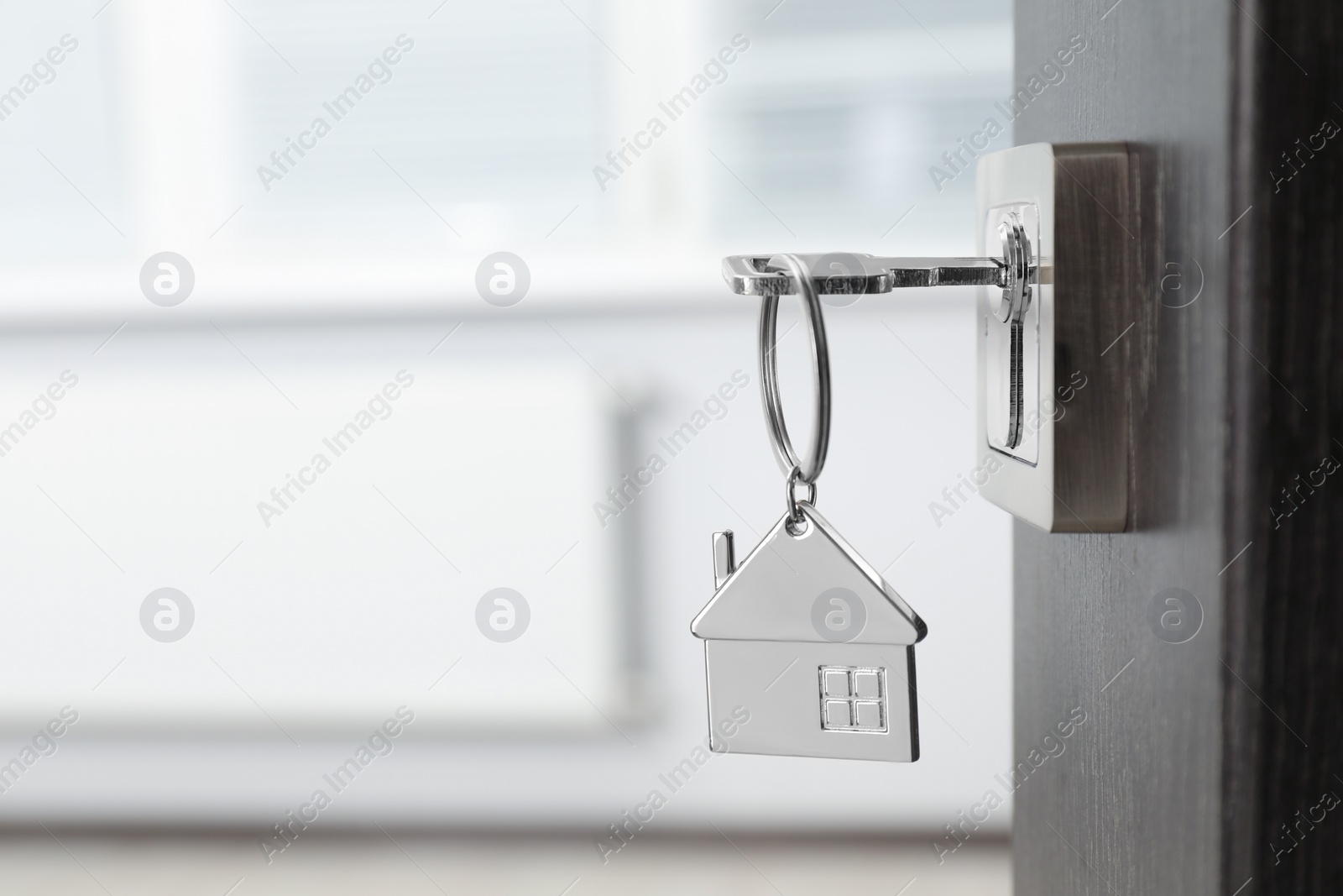 Photo of Mortgage and real estate. Open door with key and house shaped keychain against blurred background, space for text