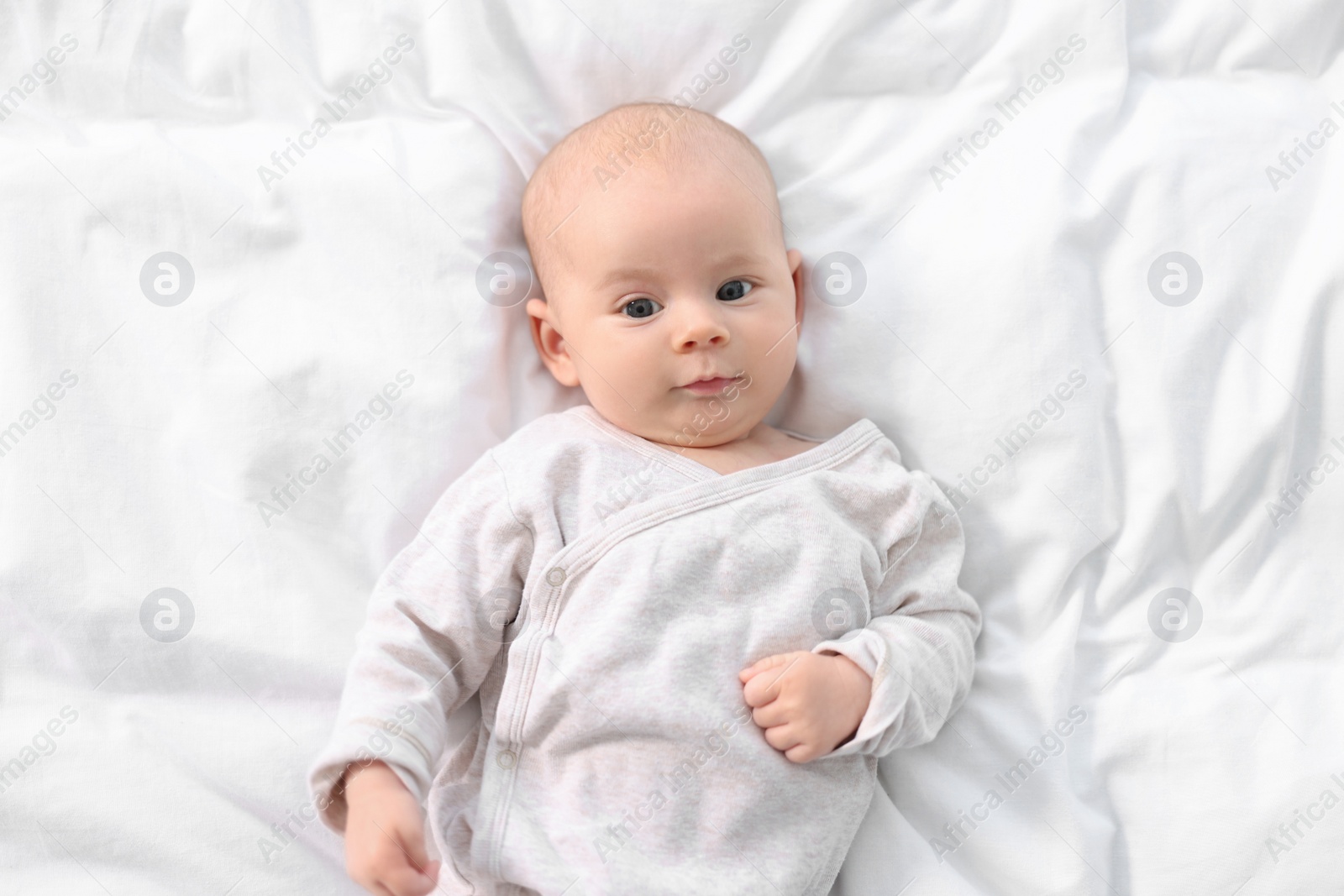 Photo of Cute little baby lying on white sheets, top view