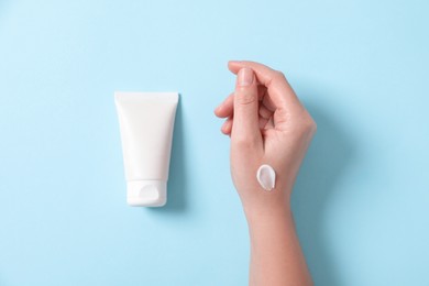 Woman with tube of hand cream on light blue background, top view