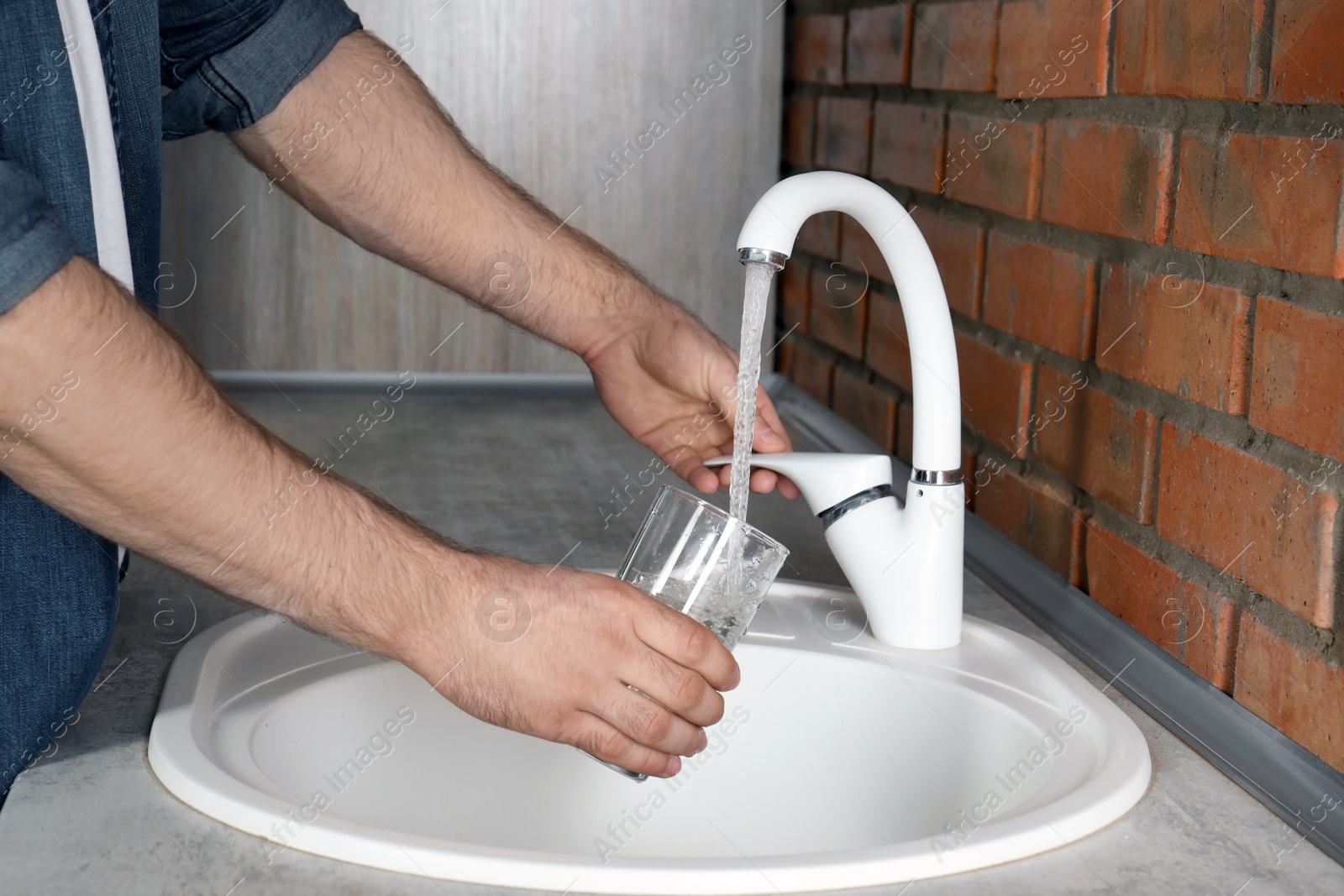 Photo of Man filling glass with water from faucet in kitchen, closeup