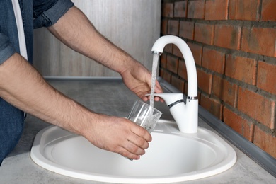 Man filling glass with water from faucet in kitchen, closeup