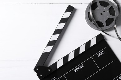 Photo of Clapperboard and film reel on white wooden table, flat lay. Space for text