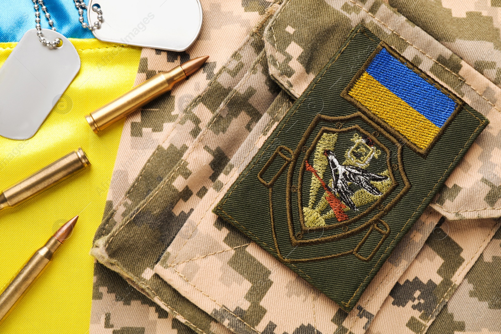 Photo of Ukrainian military uniform with chevron, bullets and ID tags on national flag of Ukraine, flat lay