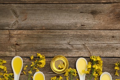 Photo of Rapeseed oil in bowl, gravy boats and beautiful yellow flowers on wooden table, flat lay. Space for text