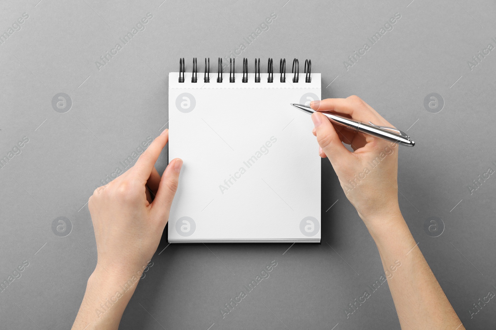 Photo of Woman writing in notebook on grey background, top view