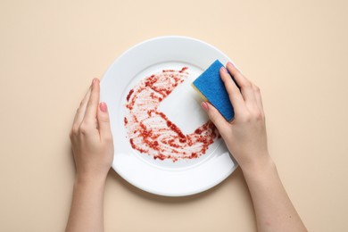 Photo of Woman washing dirty plate with sponge on beige background, top view