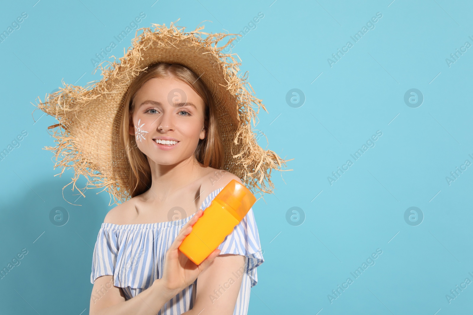 Photo of Beautiful young woman in straw hat with sun protection cream on light blue background, space for text