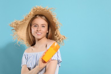 Beautiful young woman in straw hat with sun protection cream on light blue background, space for text