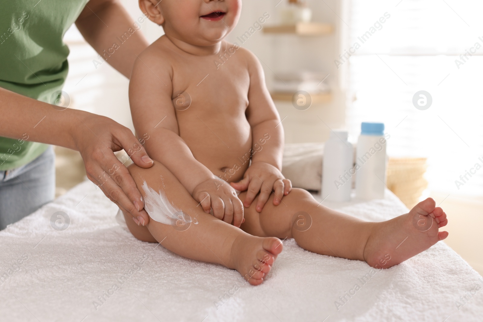 Photo of Mother applying body cream on her little baby at home, closeup