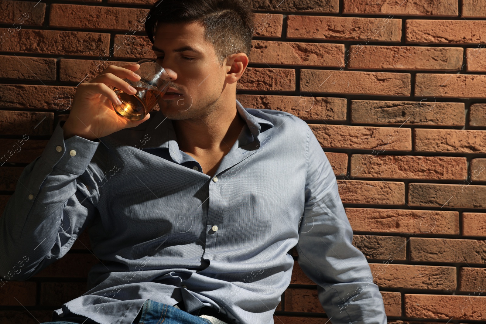 Photo of Addicted man drinking alcohol near red brick wall