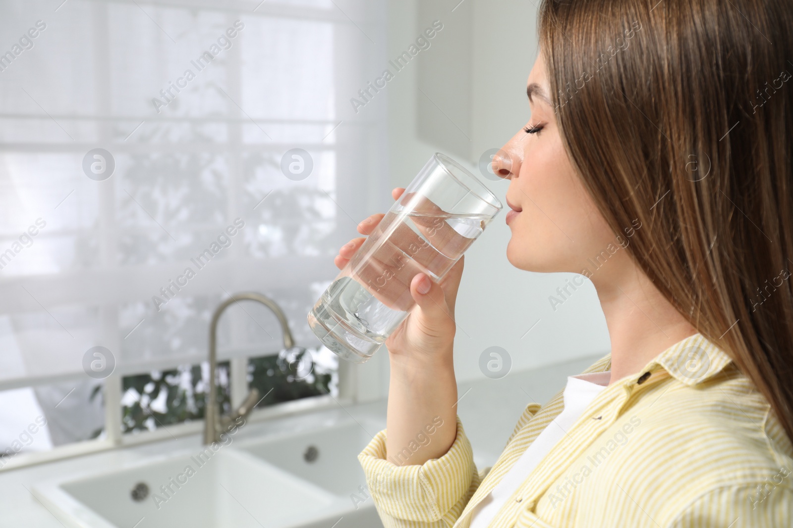 Photo of Woman drinking tap water from glass in kitchen