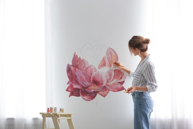 Photo of Decorator painting flower on white wall in room. Interior design