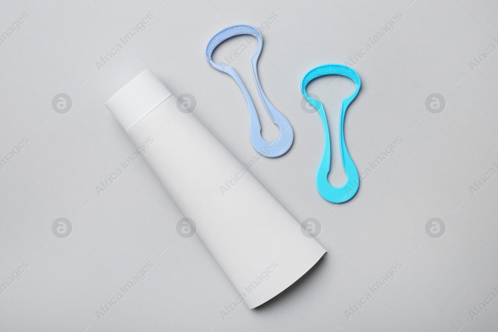 Photo of Tongue cleaners and tooth paste on grey background, flat lay