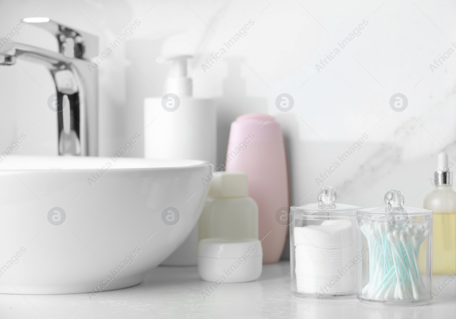 Photo of Containers with cotton swabs and pads near cosmetic products on white countertop in bathroom