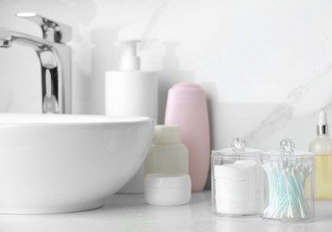 Photo of Containers with cotton swabs and pads near cosmetic products on white countertop in bathroom