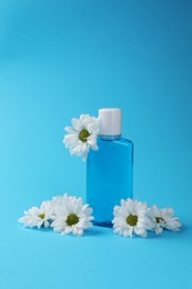 Fresh mouthwash in bottle and flowers on light blue background