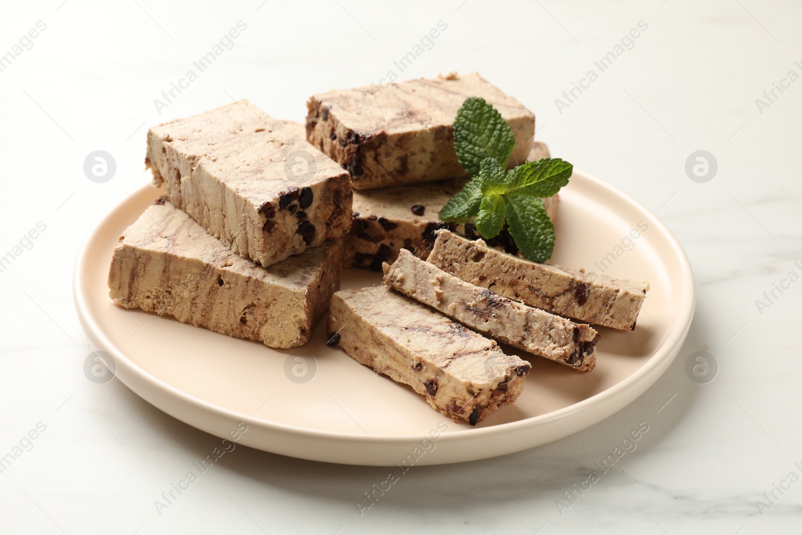 Photo of Pieces of tasty chocolate halva and mint on white marble table, closeup