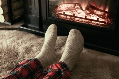 Photo of Man in knitted socks resting near fireplace at home, closeup of legs