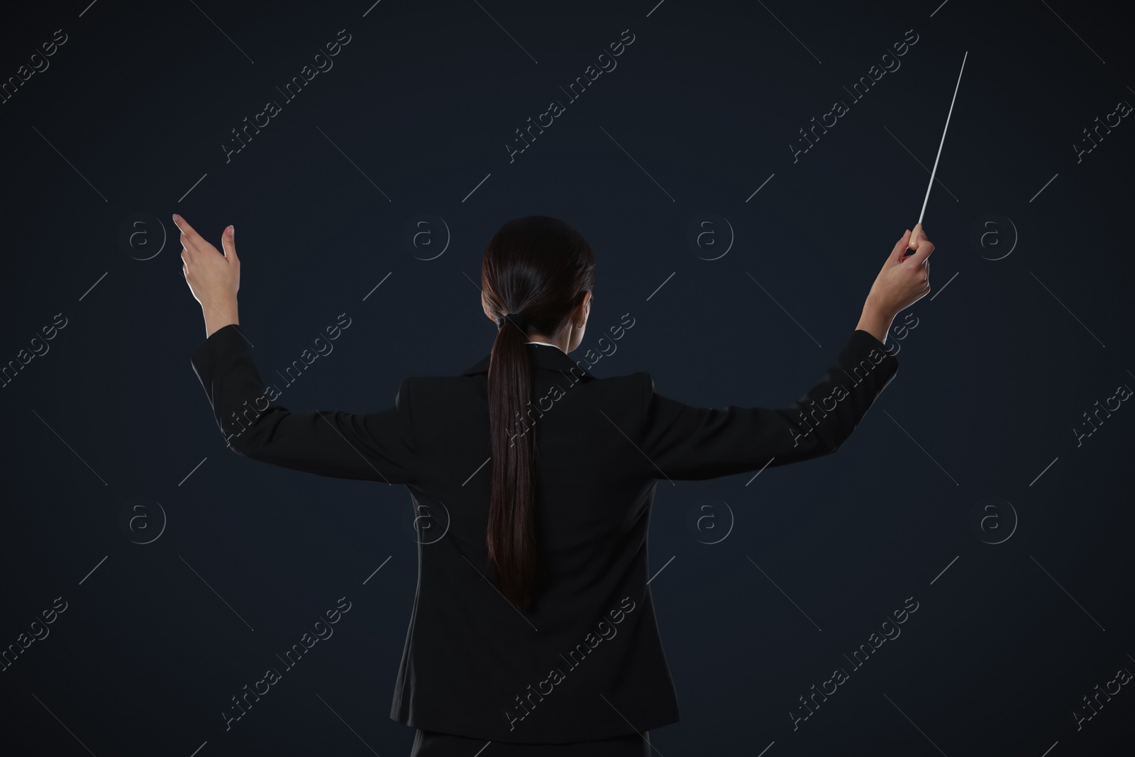 Photo of Professional conductor with baton on dark background, back view