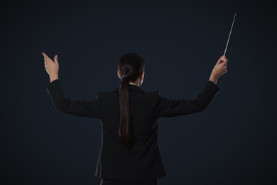 Professional conductor with baton on dark background, back view