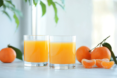 Glasses of fresh tangerine juice and fruits on white wooden table