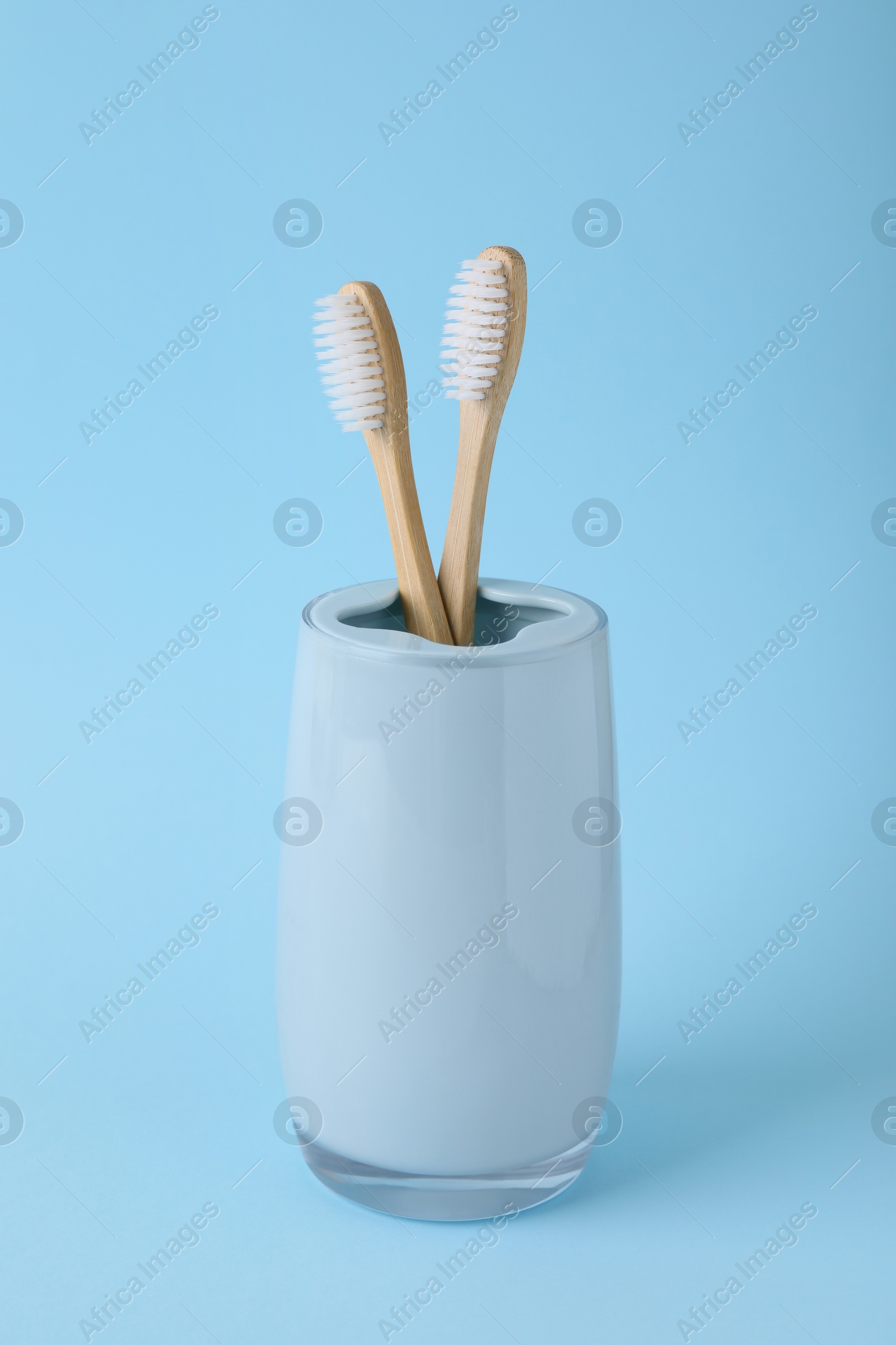 Photo of Bamboo toothbrushes in holder on light blue background