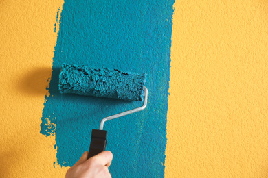 Photo of Man painting yellow wall with blue dye, closeup