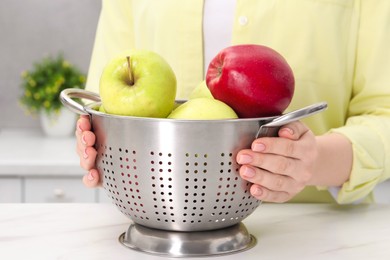 Photo of Woman holding colander with fresh apples at white marble table in kitchen, closeup