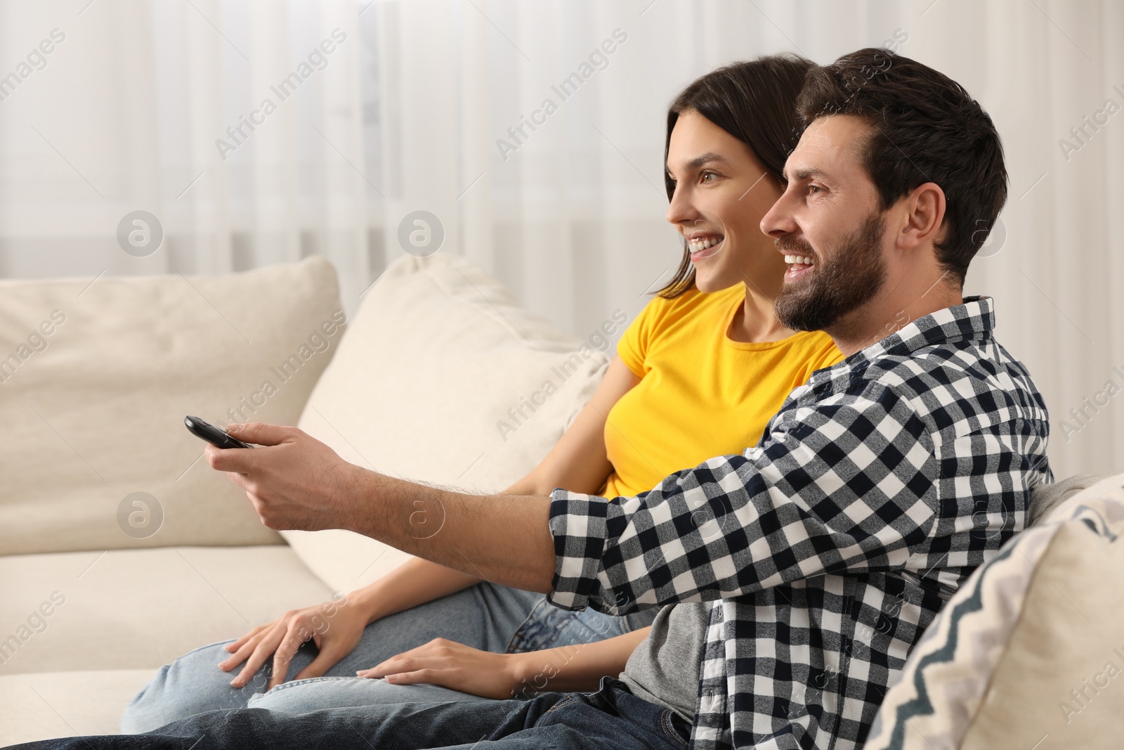 Photo of Happy couple watching TV on sofa at home